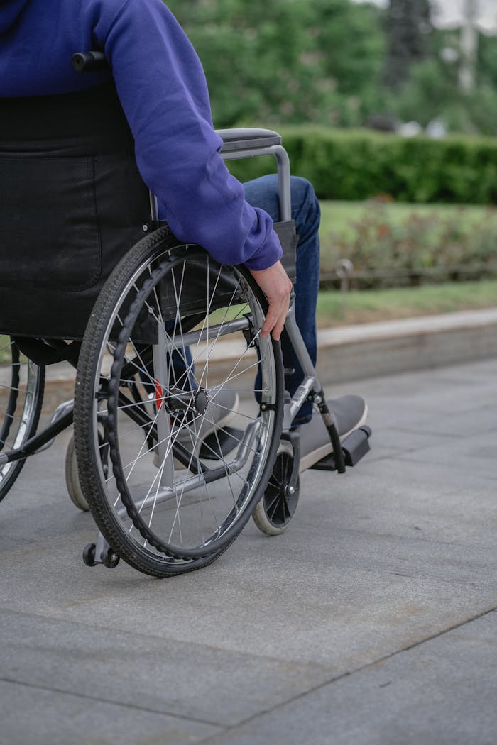 Home Individual in a wheelchair on a paved walkway outdoors, showcasing mobility and independence.